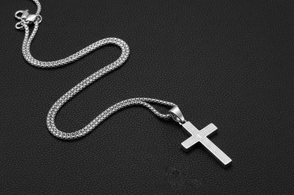 Silver cross necklace laid differently on black leather